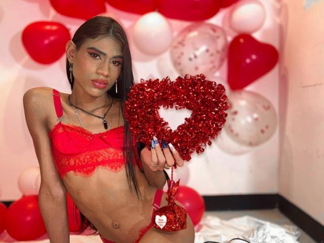 LissyAndrade with long black hair, red lace bra and panties, holding a red glitter heart, sitting in a room with red and white balloons, showing a slim, cute, tiny-ass.