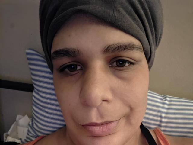 CockTease has a cute, chubby face with brown eyes, a gray headwrap, and a small smile. Her pink lips are slightly puckered. She's wearing an orange tank top.
