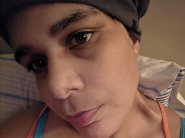 CockTease has a dark headwrap, brown eyes, and pink lips, with a slight smile. She's wearing a blue tank top, showing a small bit of her tits.