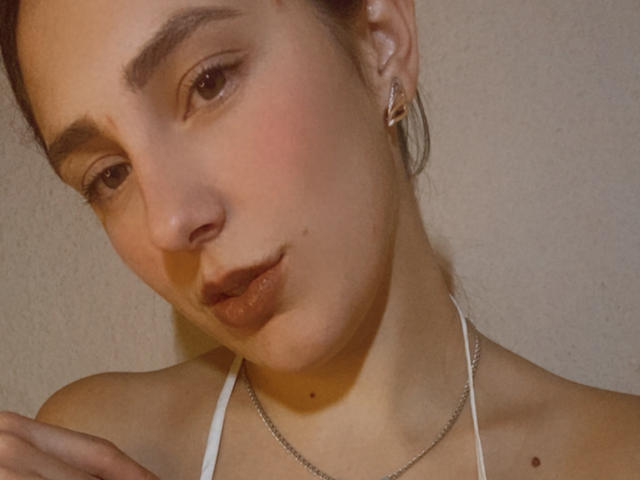 MelisseX has a cute, pouty face with brown eyes, light skin, small nose, and slightly flushed cheeks. She's wearing a white halter top and a silver necklace.