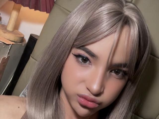 KateGoddes has shiny blonde hair, full pink lips, and thick black eyeliner. She's looking at the camera with a slight pout. Her ass is not visible.