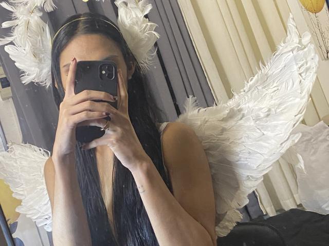 CassandraWise with white angel wings, taking a mirror selfie with a black phone, covering her face, long black hair, and a black top, showing her tits slightly.