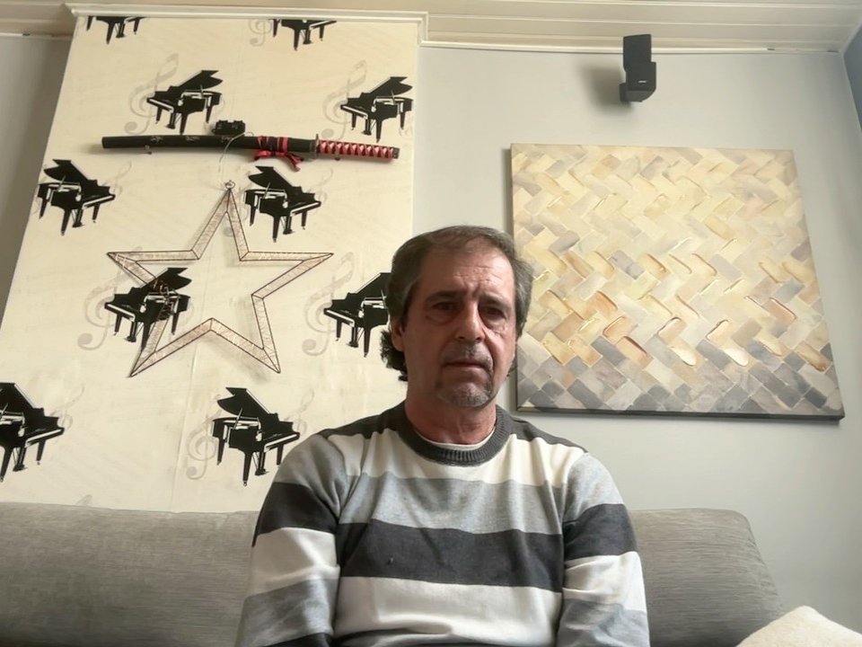 TophiePhy, middle-aged guy with gray-striped sweater, short gray hair, and slight beard, sitting on gray couch, looking tired, with black and red katana on wall behind.