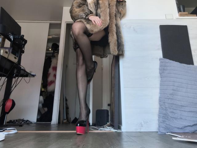 OrianaLaFrancaise in black sheer stockings, red platform heels, and a brown fur coat, with one leg raised, showing her ass and black high heels.