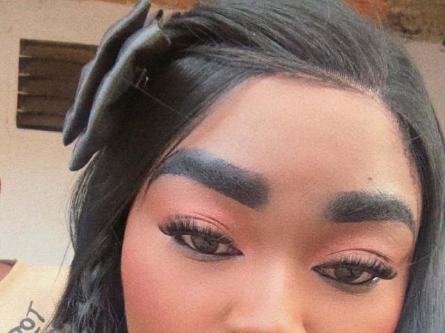 ReinaEbanox's face with dark eyebrows, thick eyelashes, and brown eyes. She has black hair with a large bow on the left side. Her skin is a warm brown tone.