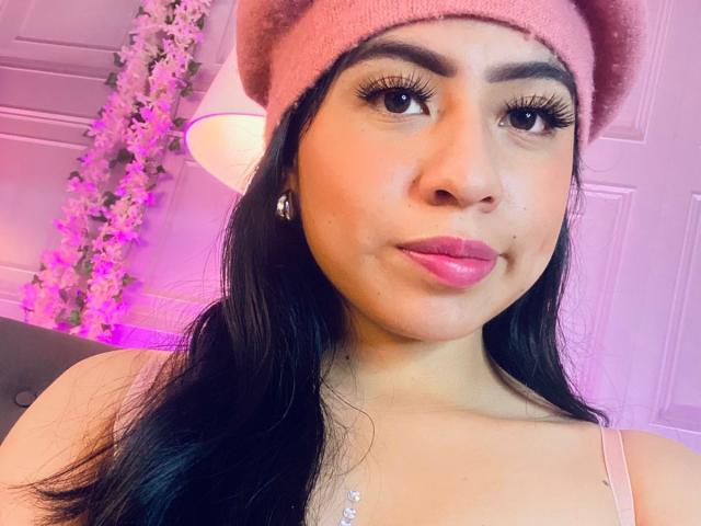 ZoeRedds with dark hair, pink beanie, and pink lipstick, showing off her pretty face and long eyelashes, wearing a pink top and a necklace, looking cute.