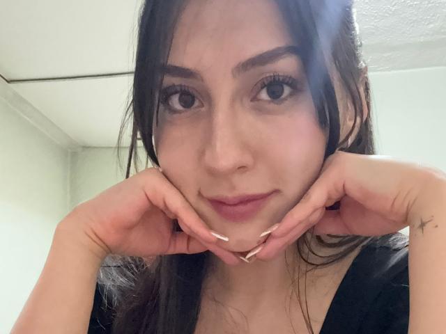 Luluberrie with dark hair, fair skin, and long eyelashes, resting her chin on her hands with a slight smile, showing off her pink-nailbed, ass-licking, tits-peeking fingers.