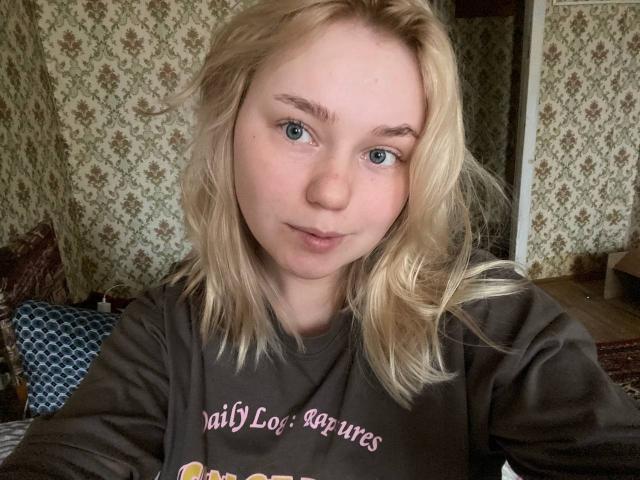 RadiantStwo with blonde hair and blue eyes, wearing a brown shirt, has a soft smile, and her nose is slightly upturned. Her tits are small and she's cute.