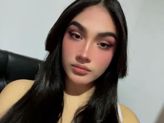 MissSubmissive hat langes, schwarzes Haar, rosigen Lidschatten und rosafarbenen Lippenstift. Ihre Augenbrauen sind dicht und sie trägt dezentes Make-up. Ihre Brüste sind nicht sichtbar, nur ihr Oberkörper..