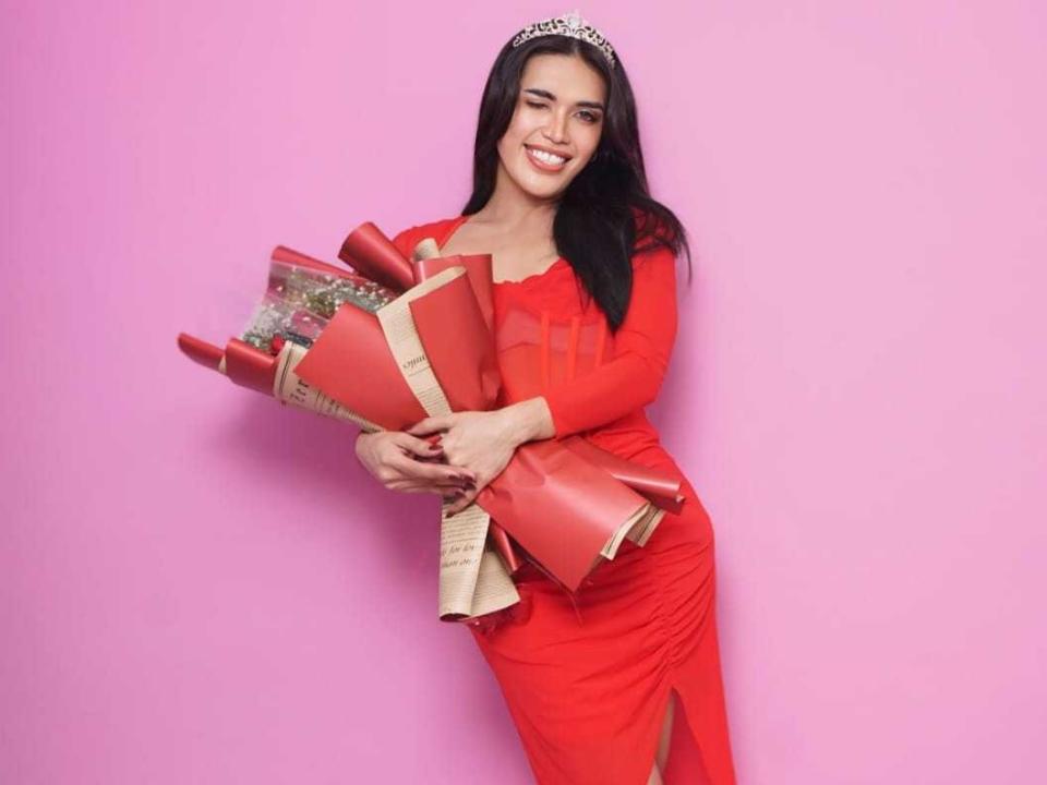 Zcin with long black hair, red dress, and tiara, holding red gift boxes, smiling, pink background. Boobs, tits, pretty, cute, attractive. Zcin's tits are small to medium.