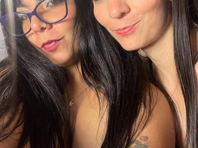 ValkiriaAndDione has black hair, wearing blue glasses, pink lipstick, and a necklace. ValkiriaAndDione's tattooed shoulder and small boobs are visible. ValkiriaAndDione's second face is slightly to the right.