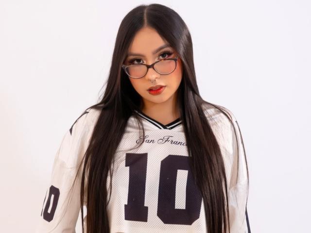 ChloeMoretti with long black hair, wearing glasses, a white football jersey with number 10, and red lipstick, looking directly at the camera.