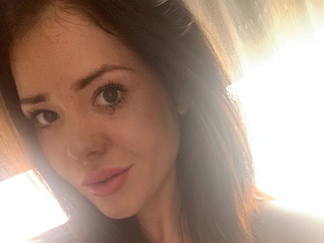 NicoleKatze-hot has brown eyes, pink lips, and a cute face with slightly wavy dark brown hair, looking at the camera with a subtle smile.
