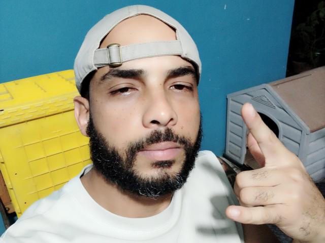 BobHas with a beige cap, dark beard, and white shirt, giving a thumbs-up, has a medium skin tone, and is sporting a slightly tired expression.