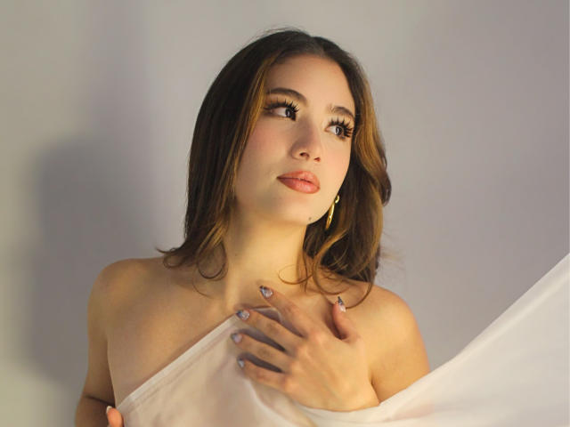 StarDustt with brown hair, nude, holding a white sheet over her tits, looking up with eyelashes, gold earrings, pink nails, soft light, gentle expression, slight smile.