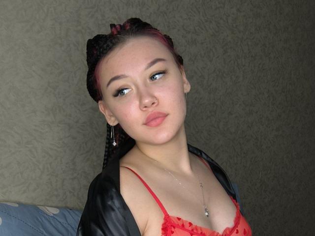 CloraFlippin with red bra, braided hair, pink highlights, nose ring, necklace, looking to the side, pouty lips, black jacket, red lace, light skin, subtle makeup, soft expression.