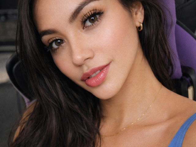 SofieWhite has brown eyes, long dark brown hair, pink glossy lips, and a small gold earring in her right ear, wearing a blue top, with a slight smile.
