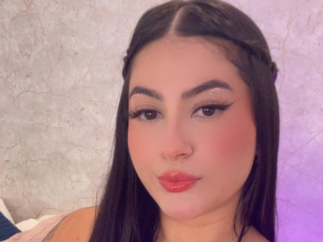 AlanaaWalker with long black hair, braided front, thick eyebrows, glittery eyeliner, pink blush, red lipstick, pouty lips, pale skin, looking at camera, soft light.