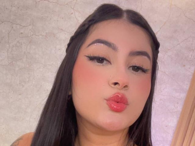 AlanaaWalker has puffy red lips, long black hair in braids, thick black eyebrows, and is puckering her ass up in a selfie with glittery eyeliner.