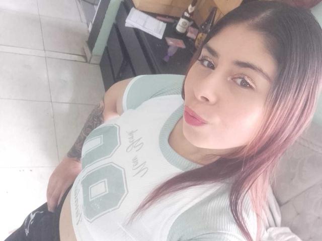 VictoriaLeclerco has pinkish-brown hair, light skin, and wears a white, green, and gray sports shirt with "00" on it, showing her small, perky tits and tattooed arm.