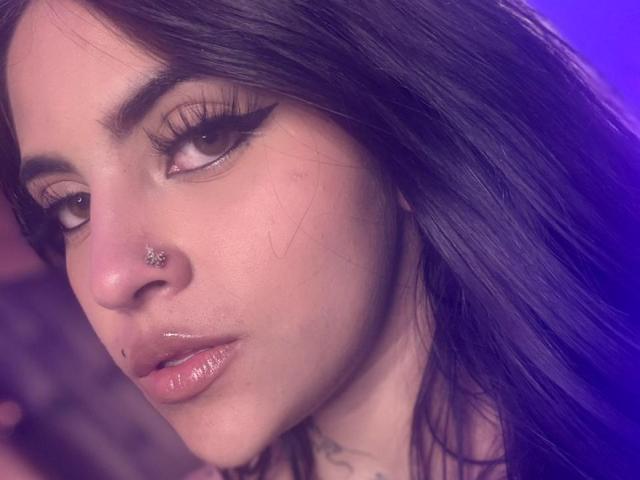 Il viso di CoriPaige, con i suoi lunghi capelli neri, gli occhi marroni, l'eyeliner spesso, le labbra rosa lucide, un piccolo anello d'argento al naso e una piccola lentiggine vicino al labbro superiore..