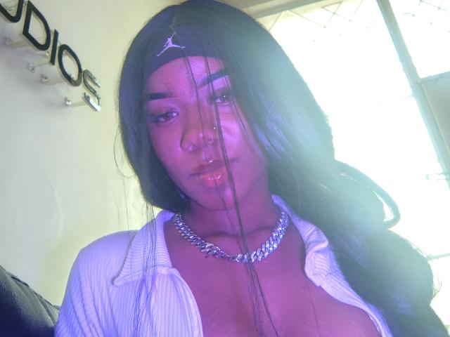 SophiaTaylorn with long black hair, purple eyeshadow, white open shirt, and silver chain necklace, showing her tits and nose ring, looking into the camera with a slight pout.