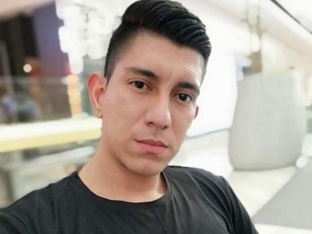 SanderNoah has a serious face, short black hair, and a black shirt. His nose is slightly upturned and he has a small nose ring on his right nostril.