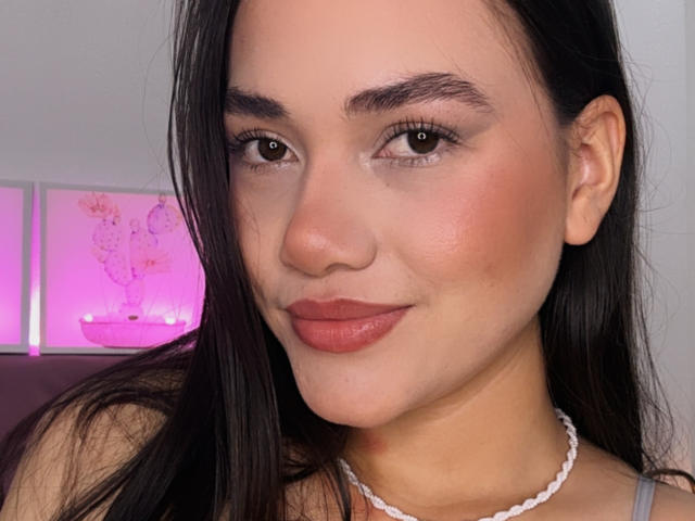 AddaS has medium brown eyes, dark brown hair, and pinkish-red lips. She wears a white beaded necklace and smiles slightly. Her skin is smooth and lightly tanned.