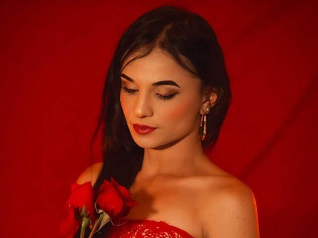 PamelaKander with red rose, holding against her tits, dark hair, red lipstick, closed eyes, earrings, red dress, red background, soft lighting, sensual, attractive, sexy.