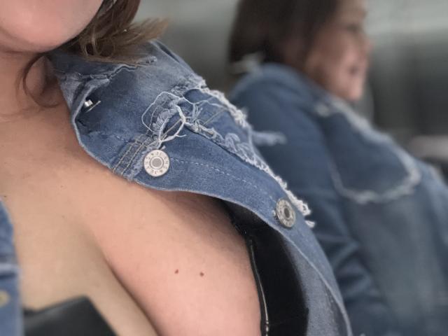SophiaQueens' denim jacket is partially open, revealing her bare shoulder and black strap, with a small mole visible. Reflection shows her face in the background.