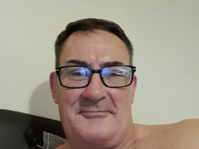 StillGold, shirtless with glasses, has a slightly sweaty face, short dark hair, and a small smile. His ass is not visible, but his upper chest is shown.