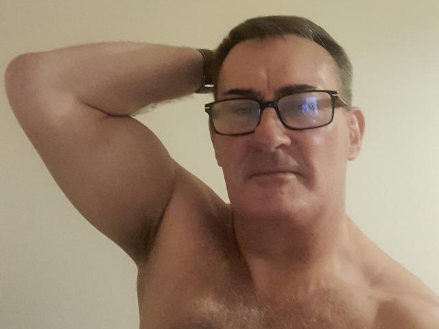 StillGold, shirtless, with a muscular arm raised, wearing glasses, has a slightly annoyed expression, and is showing a hairy armpit. His chest is also hairy.