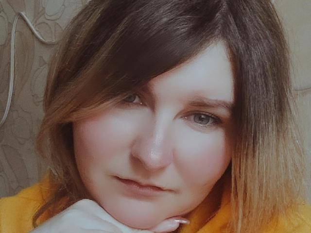 MinistraX's face with pinkish cheeks, light brown hair, and grey eyes, wearing a yellow top, resting her chin on her hand, looking slightly sad.