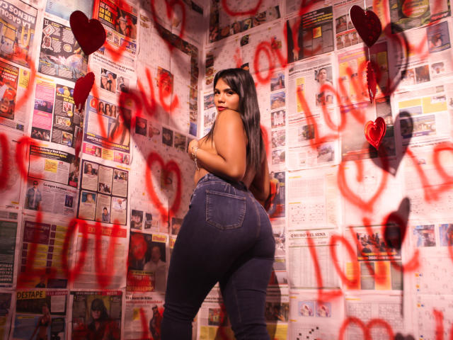 LissReyess has long black hair, big ass in tight blue jeans, and is looking over her shoulder, showing her back and red lips, surrounded by red hearts and graffiti.