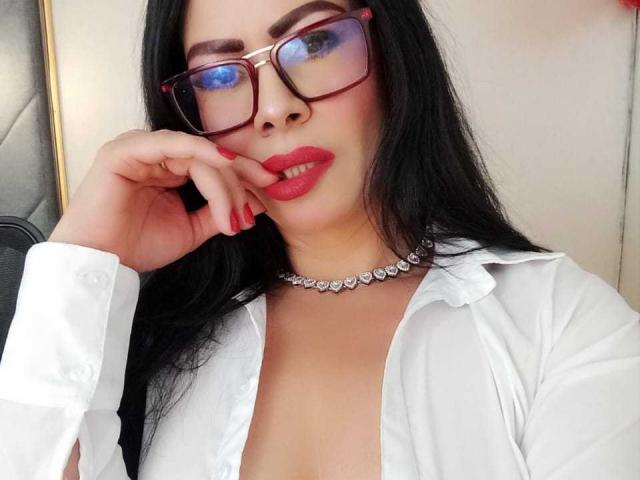 SofiMontes with red lipstick, black hair, glasses, white shirt, open chest, diamond choker, and red nails, touching her cheek, showing her tits slightly.