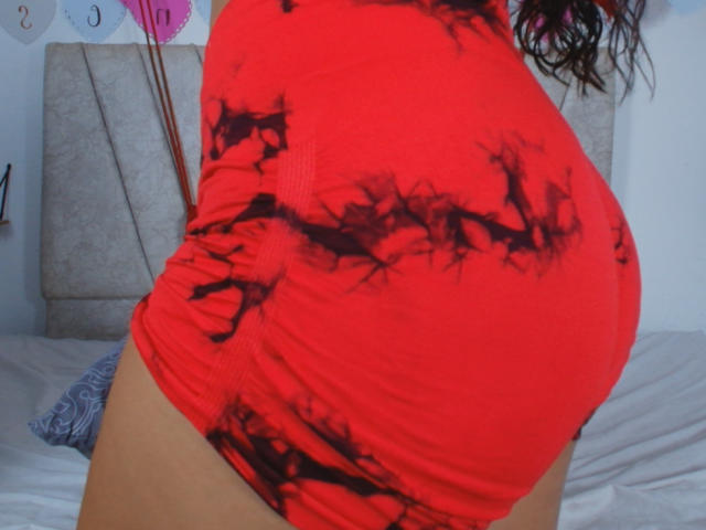 LianaAndAsaff's red, tight, black-ink-patterned butt shorts, highlighting her curvy, round ass, with wavy brown hair in the background.