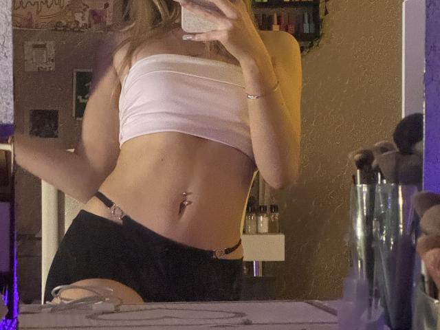 AmilySunray with a slim, flat-stomached body, wearing a pink tube top, black shorts with metal rings, and a navel piercing, taking a mirror selfie.