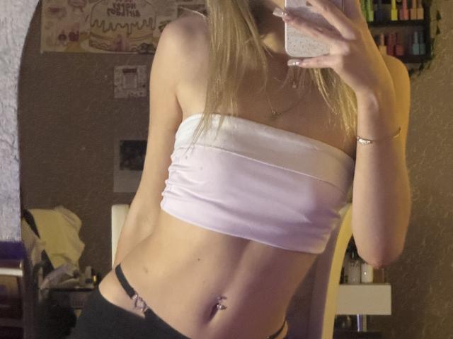 AmilySunray with blonde hair, wearing a pink tube top, black thong, and a belly button piercing, taking a mirror selfie, showing her small tits and slim waist.