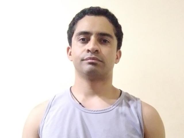 RamsesX has short curly black hair, a light brown skin tone, and is wearing a gray sleeveless shirt, looking straight at the camera with a neutral expression.