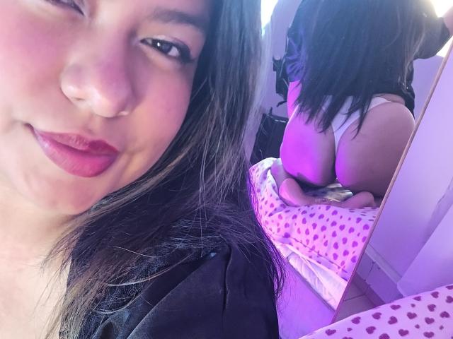 MelyOspina has a cute face with dark hair, red lipstick, and a small nose ring. Her ass is reflected in a mirror, wearing white panties.
