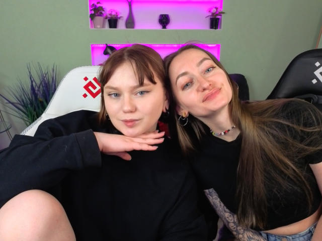 VecnanNana with short brown hair and VecnanNana with long brown hair, both in black shirts, sitting on a chair, VecnanNana's hand on neck, both smiling, purple LED lights.