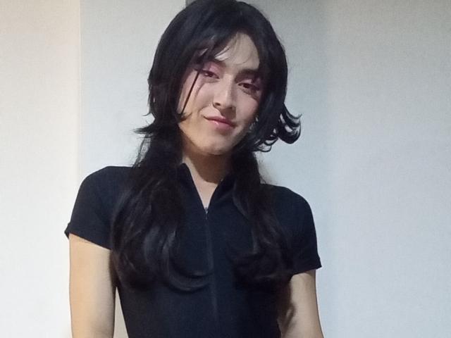 EllieCherry with long black wavy hair, wearing a black short-sleeve shirt, has a slight smile, pink eye makeup, and a cute, feminine look.