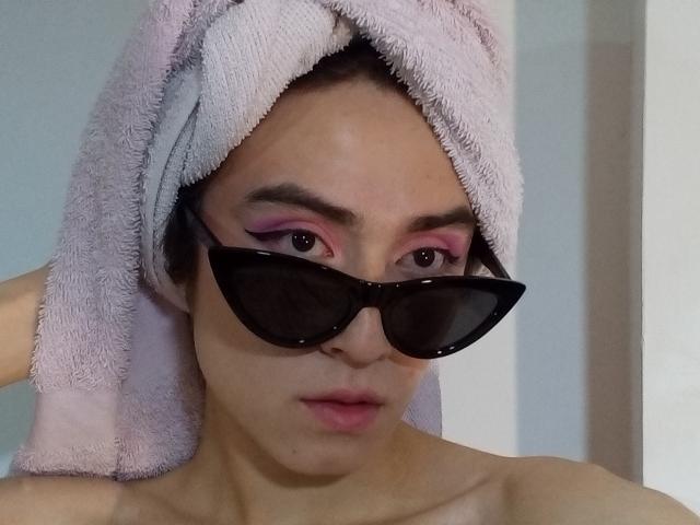 EllieCherry con una toalla rosa en la cabeza, usando gafas de sol negras y sombra de ojos rosa, mirando directamente a la cámara, con los labios ligeramente entreabiertos..