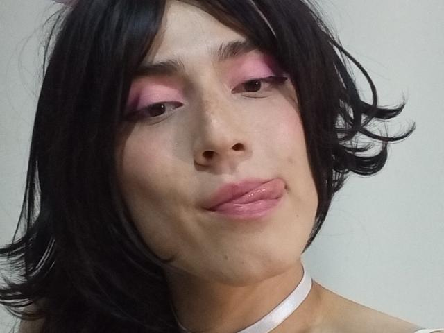 EllieCherry with black hair, pink eyeshadow, glossy pink lips, tongue slightly out, white choker, light skin, subtle freckles, soft expression, head slightly tilted.
