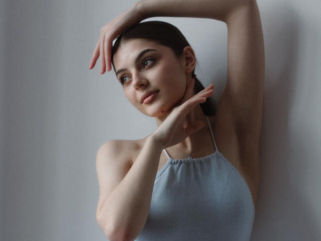 StellaLewin with arms raised, wearing a light blue halter top, showing her small tits and smooth skin, has a slight smile, and brown hair in a simple braid.