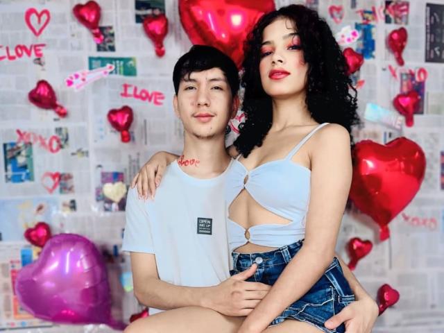 BellainLove with curly black hair, blue crop top showing tits, and denim shorts, stands next to a guy with short black hair, white tee, and hand on her ass.