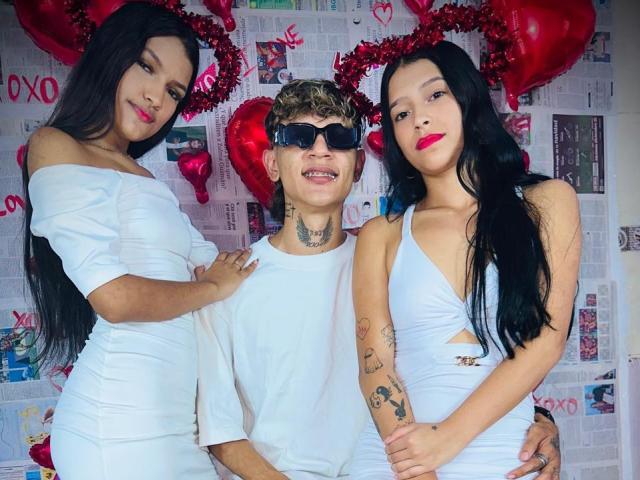 Tre persone vestite di bianco: TheXPleasure a sinistra con lunghi capelli neri e un seno pronunciato, TheXPleasure al centro con capelli biondi, tatuaggi e occhiali da sole scuri, TheXPleasure a destra..