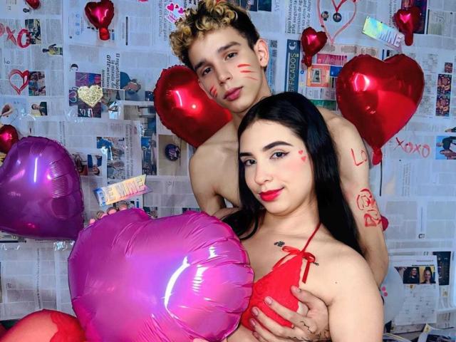 ArdienteCouple with curly blonde hair and ArdienteCouple with black hair, both topless, holding pink and purple heart balloons. Blonde ArdienteCouple's face is marked with red lipstick.