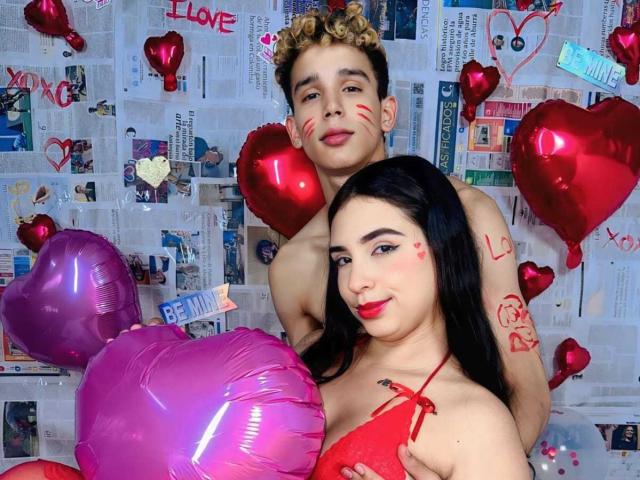 ArdienteCouple with curly hair and ArdienteCouple with black hair, both with red face paint, red hearts, and balloons, ArdienteCouple's red top, ArdienteCouple's chest in foreground.