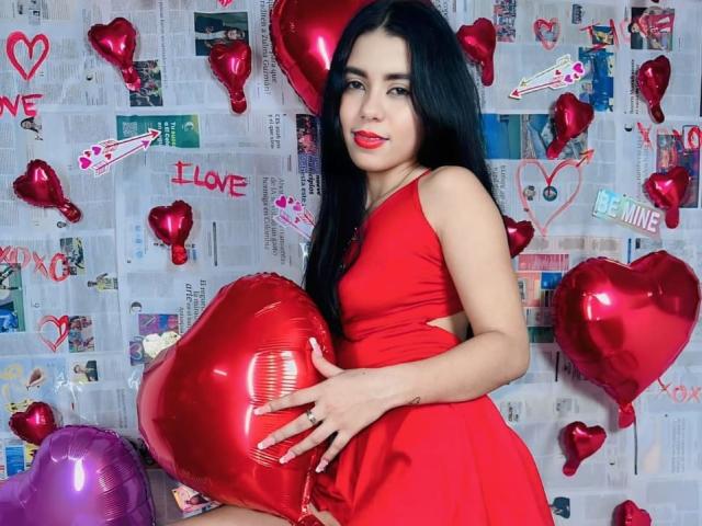InocentLooks with long black hair, red dress, holding shiny red heart balloon, red lips, cute, standing, holding heart, purple balloon bottom, red balloons scattered, looking at camera.